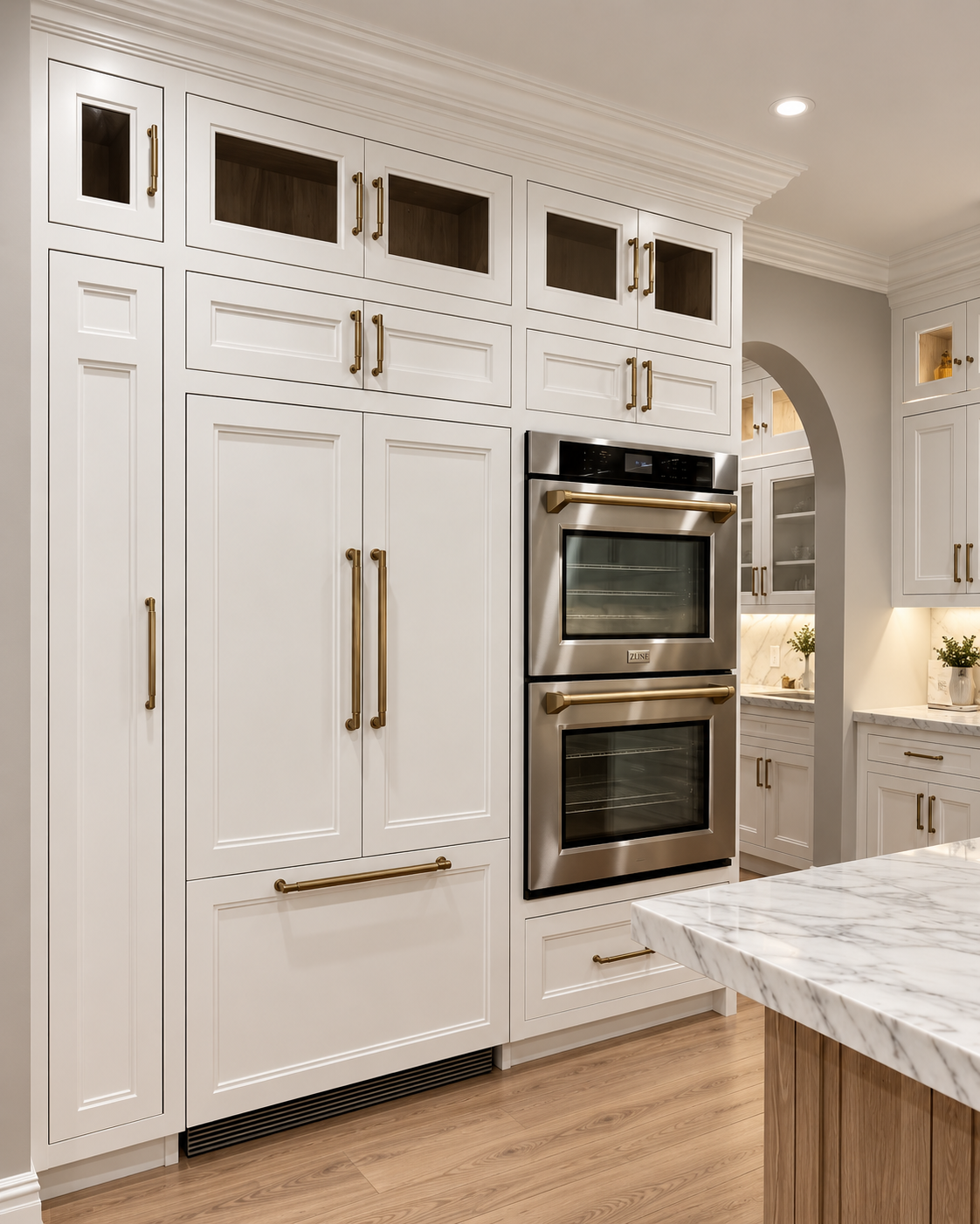 Floor-to-ceiling white custom kitchen cabinetry with brass hardware and integrated double ovens.